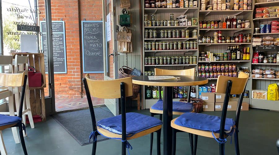 Tables and chairs inside the deli, shelves of jars behind