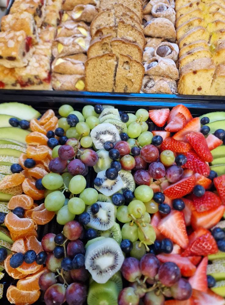 A platter of fresh fruit next to a platter of cakes