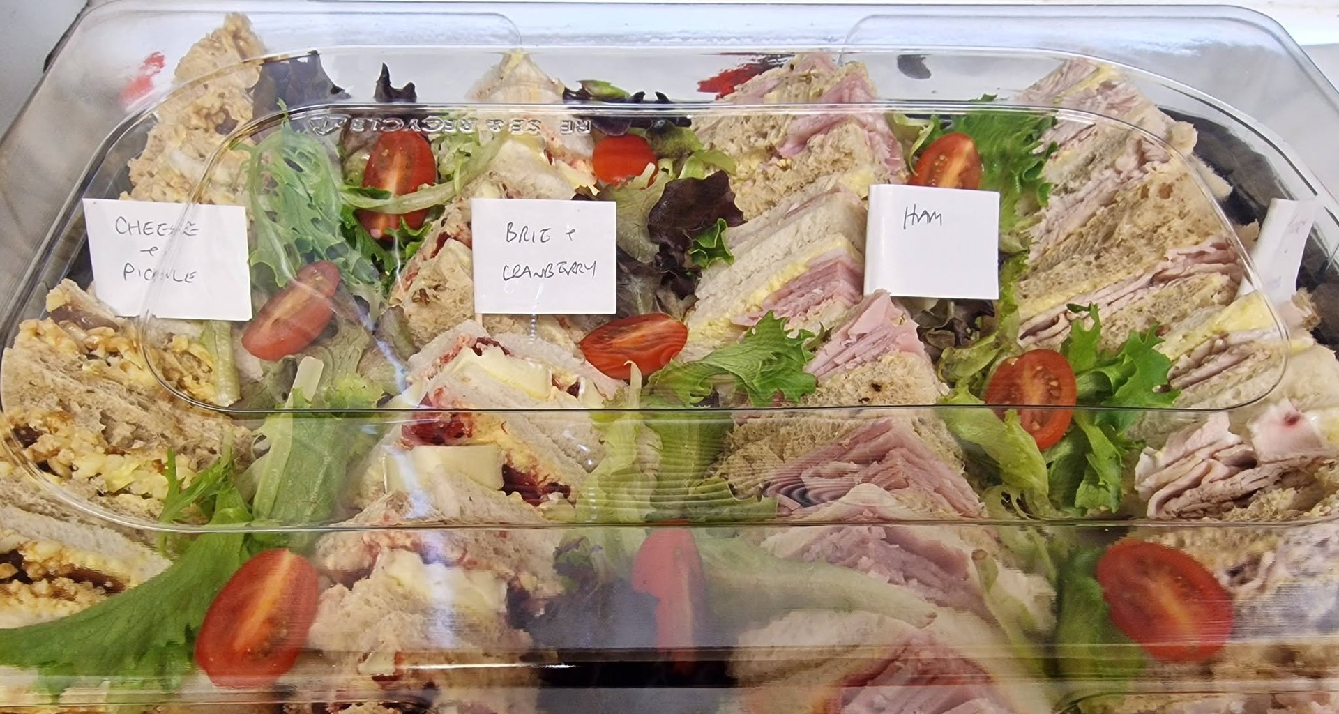 A platter of sandwiches labelled cheese and pickle, brie and cranberry, and ham
